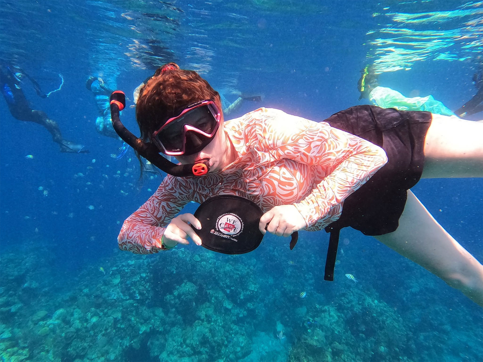 Student snorkeling while holding a COEHP We Care sign